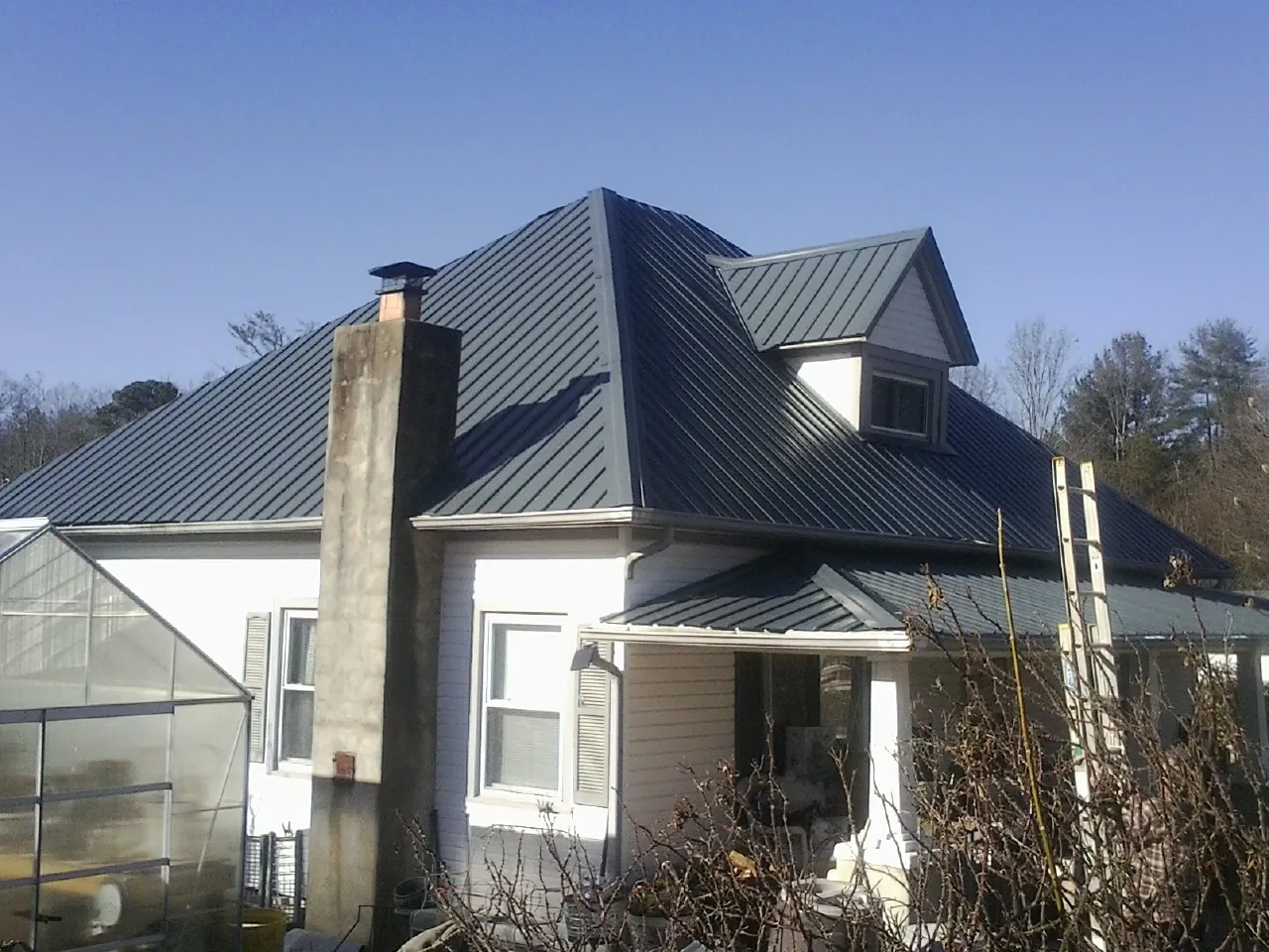 Dark blue standing seam metal roof on a white farmhouse with dormer — Slate & Tile Roof Repair by Roofing Brothers in Saint Catharine