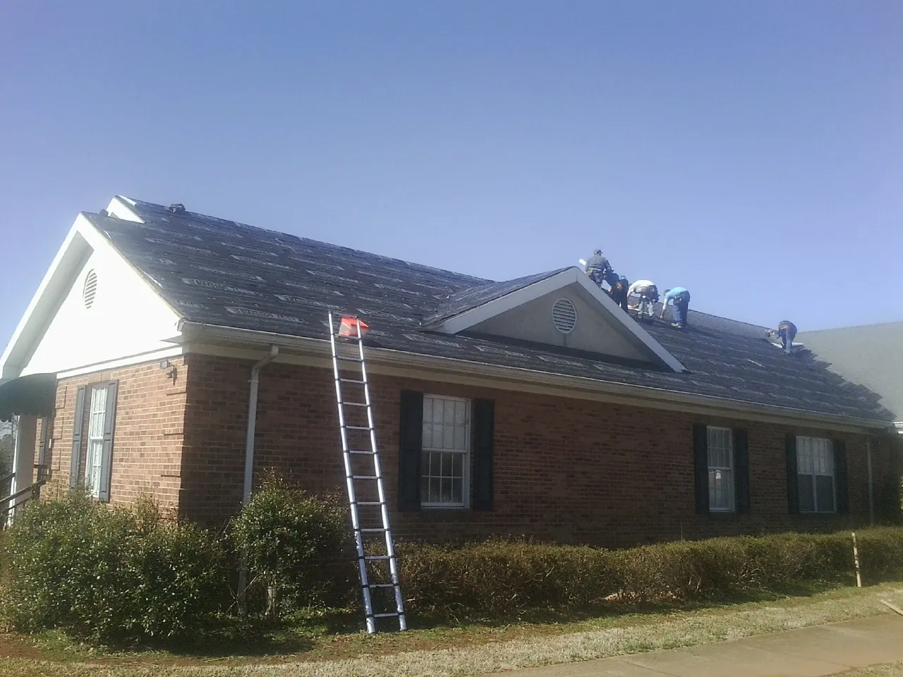 Crew tearing shingles off a brick ranch roof with a ladder set — Metal Roof Repair work by our crew in Saint Catharine