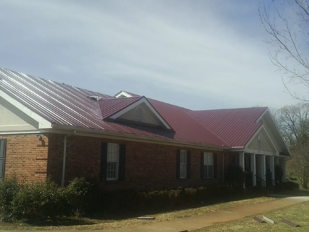 Red metal roof with gabled entries on a long brick building, from a Hail Damage Roof Repair job in Saint Catharine