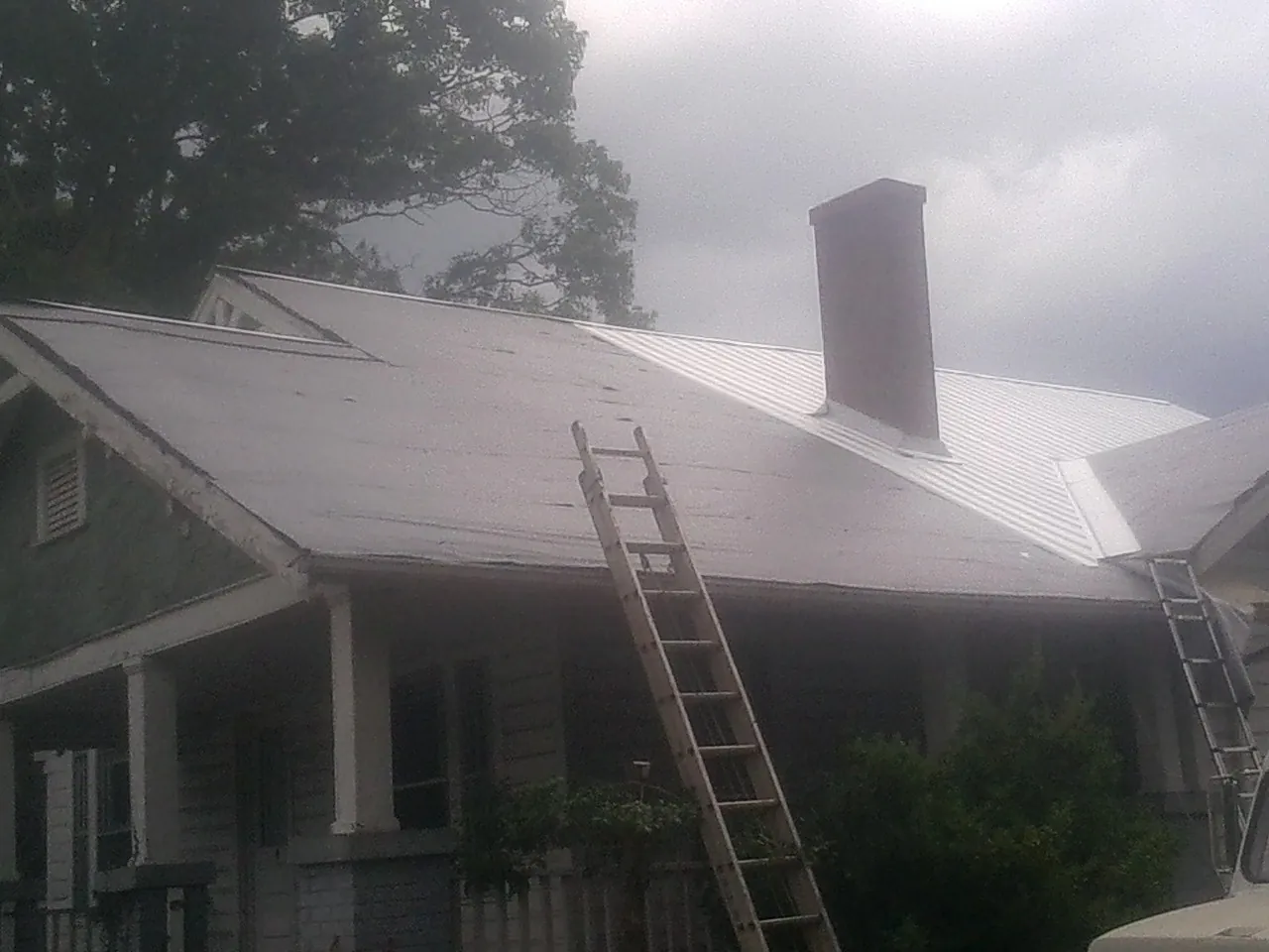 Ladders against a metal roof on an older home with a brick chimney in Saint Catharine