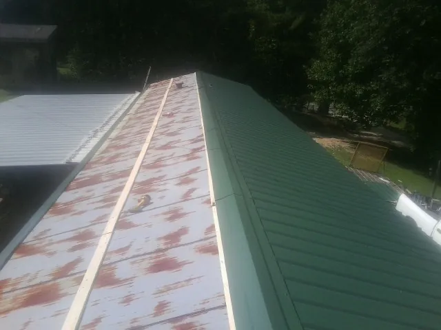 Old rusted panels beside newly installed green metal roofing — Wind Damage Roof Repair by Roofing Brothers in Saint Catharine