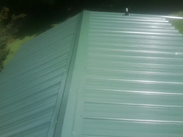 New green metal panels meeting at the ridge of a roof — Flat Roof Repair work by our crew in Saint Catharine