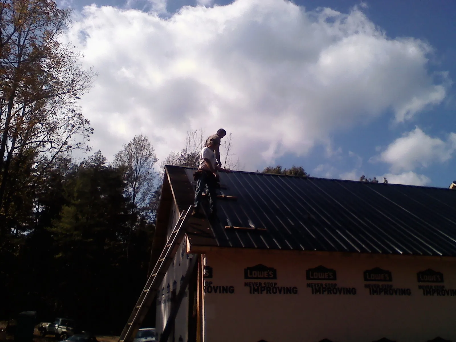 Roofer fastening dark metal panels high against a cloudy sky, from a Roof Inspection job in Saint Catharine