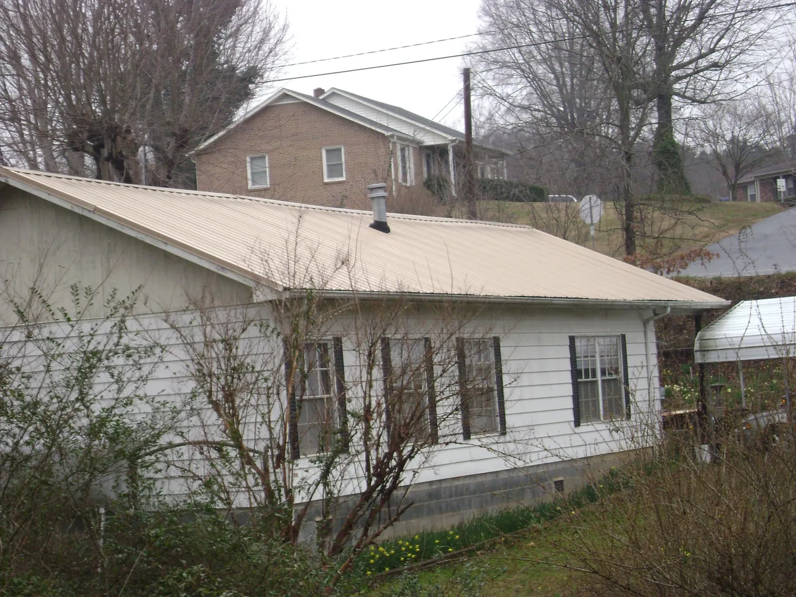 Tan metal roof on a white sided house set into a hillside — Commercial Roofing by Roofing Brothers in Saint Catharine