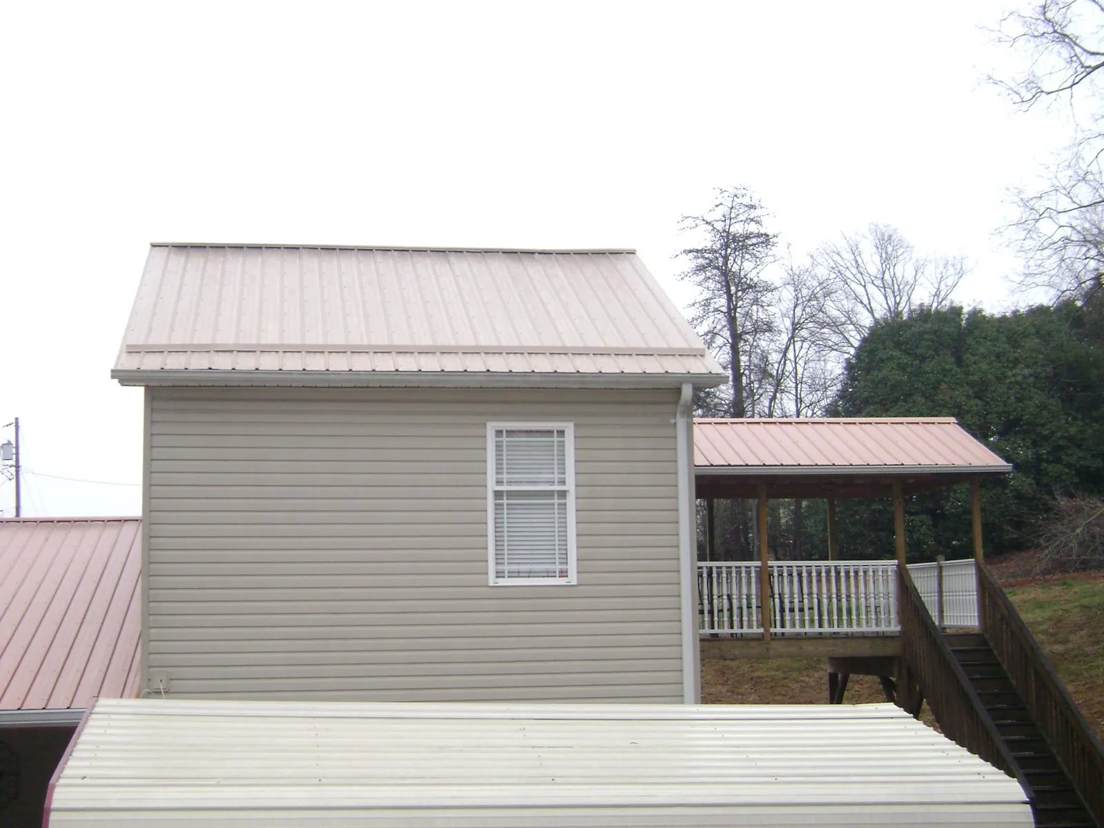Tan metal roofs on a two story addition and attached porch, from a Roof Replacement job in Saint Catharine